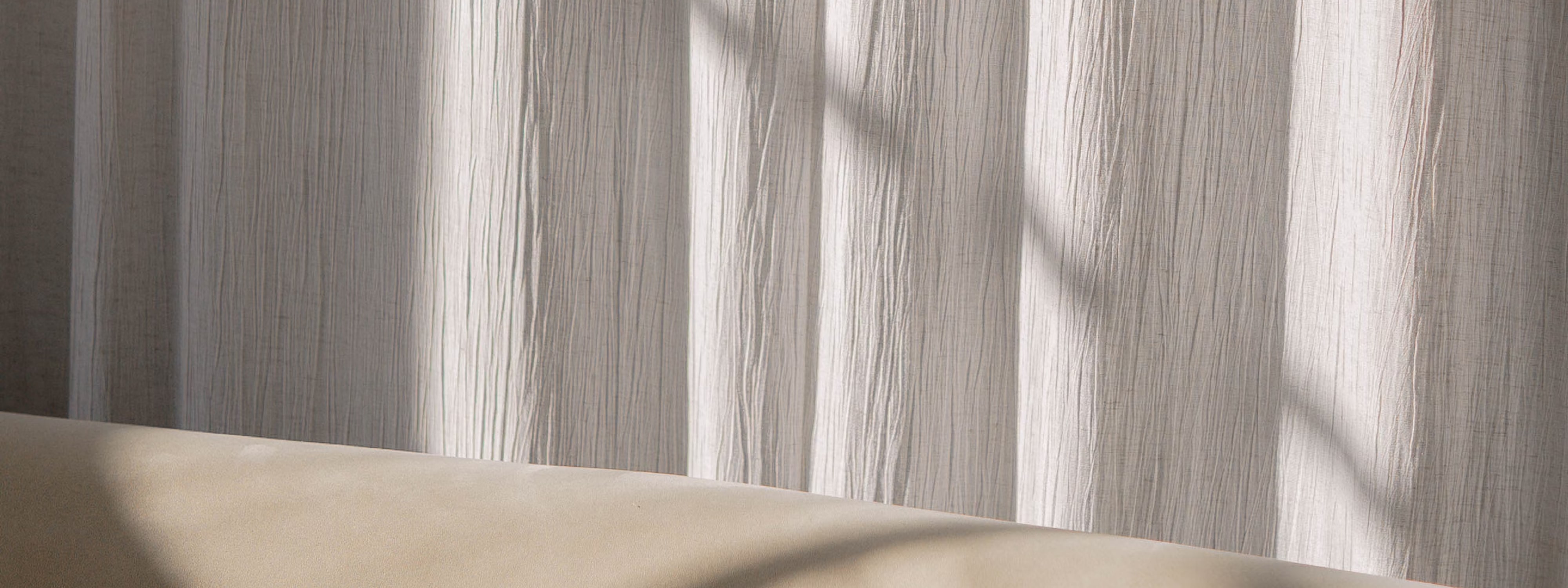 Soft light filtering through textured white curtains onto neutral surface