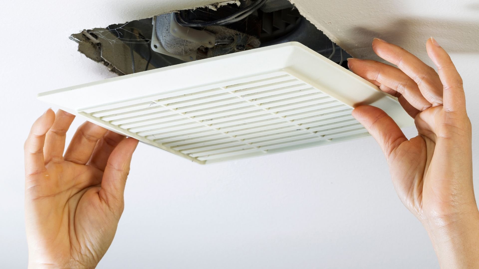 Hands installing a white ventilation or air return grate in ceiling