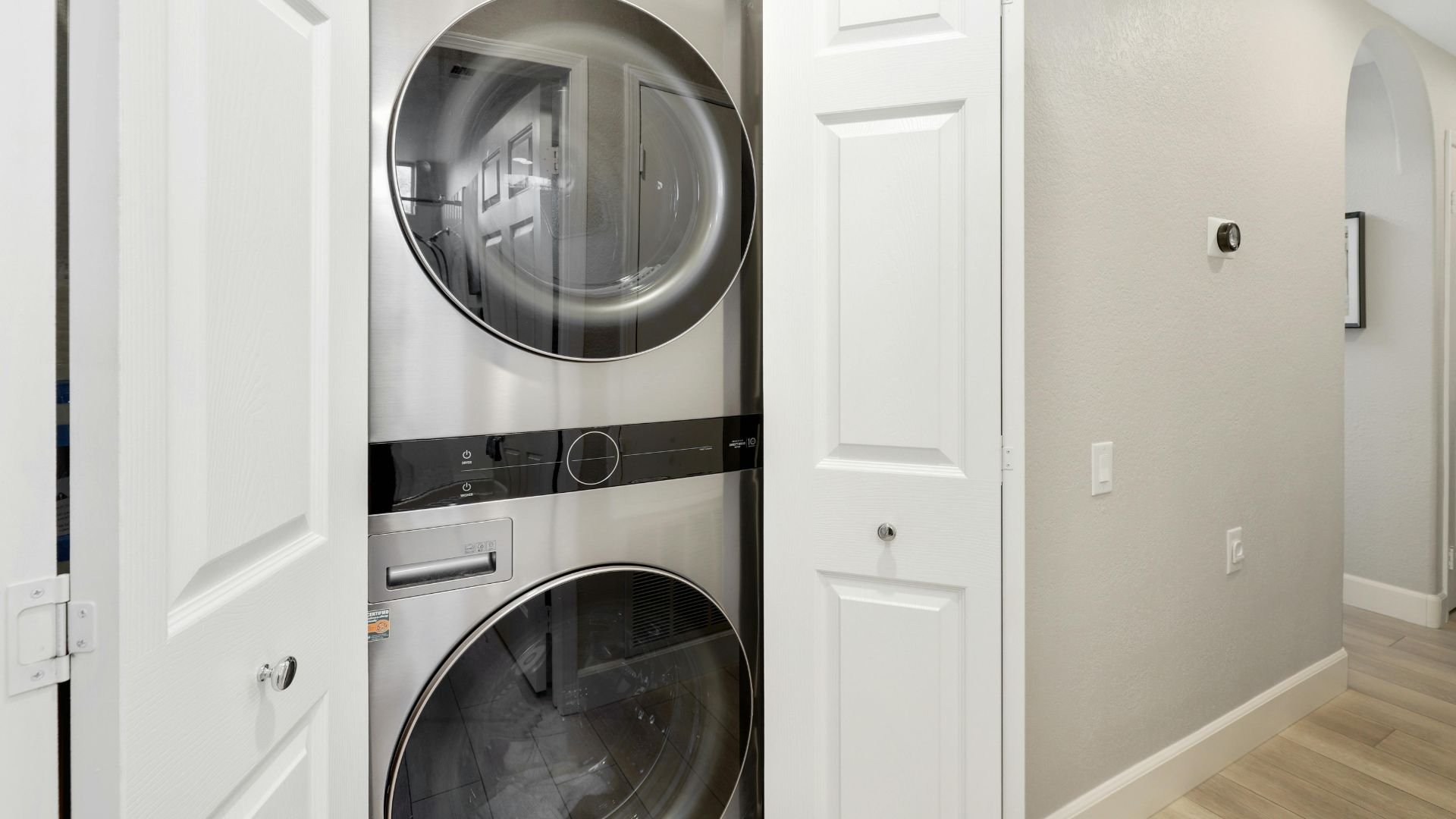 Modern stacked washer and dryer in white closet with closed doors