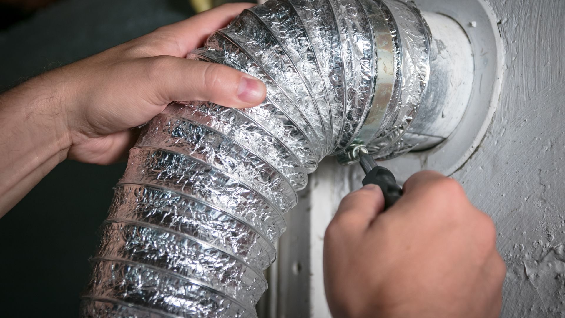 Flexible metallic dryer vent hose being attached to wall by hand